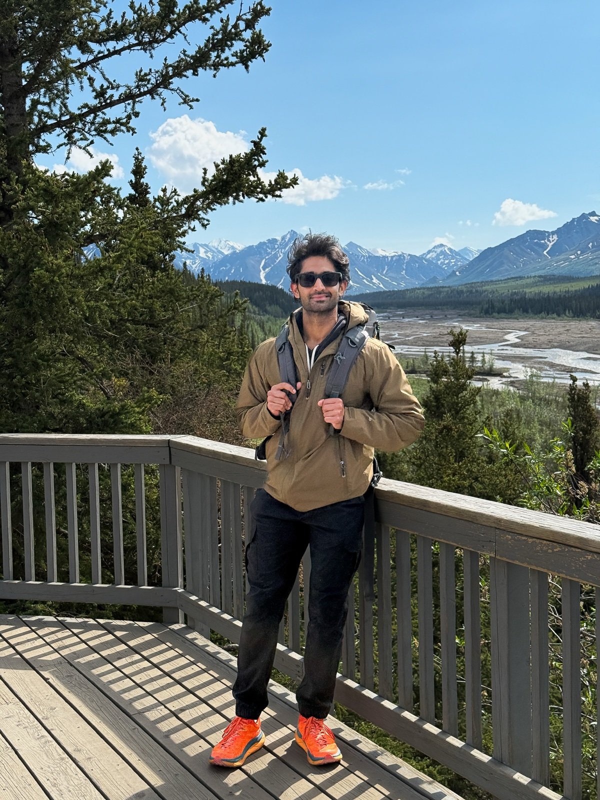 Varun Prakash standing on an overlook deck with mountains and a braided river valley behind him.